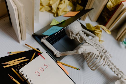 Dramatic still life of a skeleton overwhelmed at an untidy office desk with S.O.S. note.